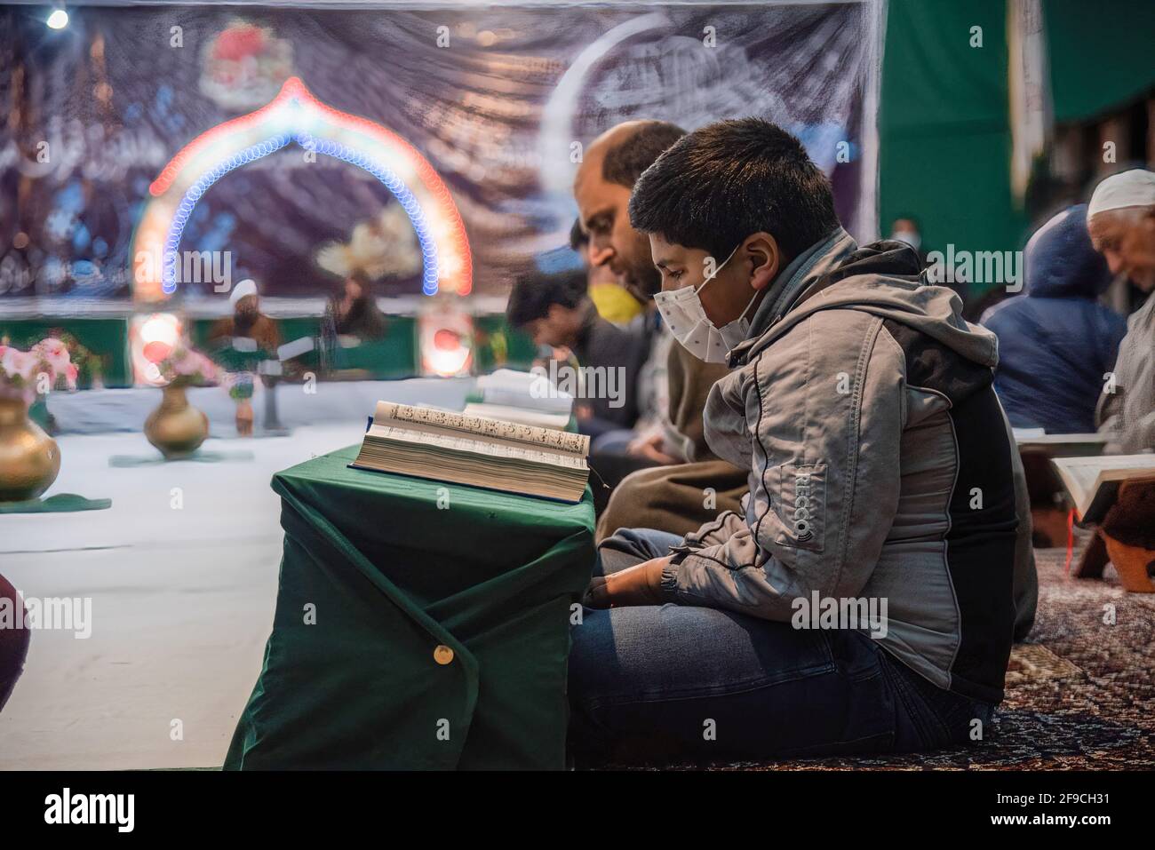A Kashmiri Muslim boy wearing a face mask recites the Islamic Holy book ...