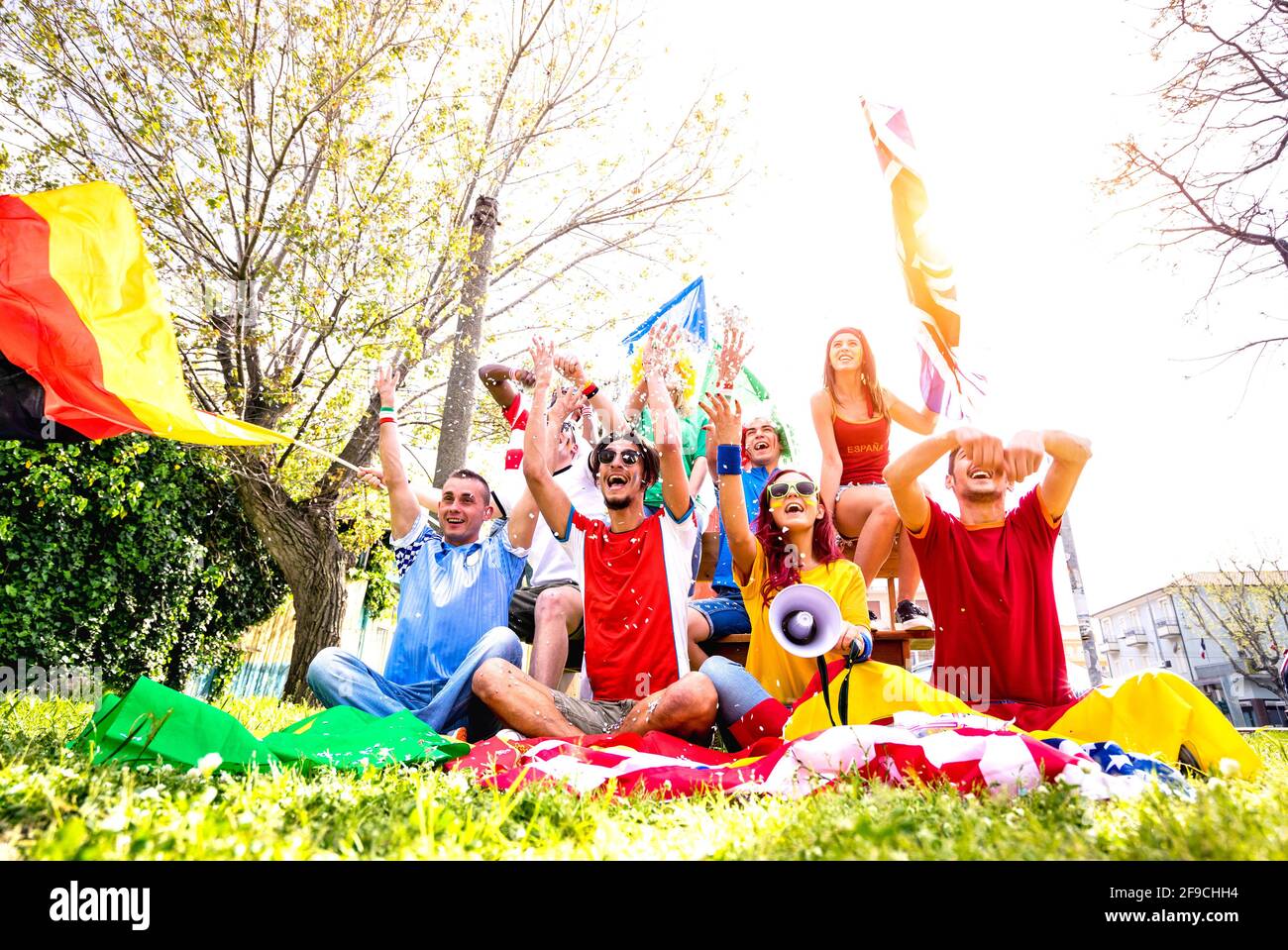 Young football supporter fans cheering with international flags at soccer match - Friends people with multicolored tshirts and flags having fun Stock Photo