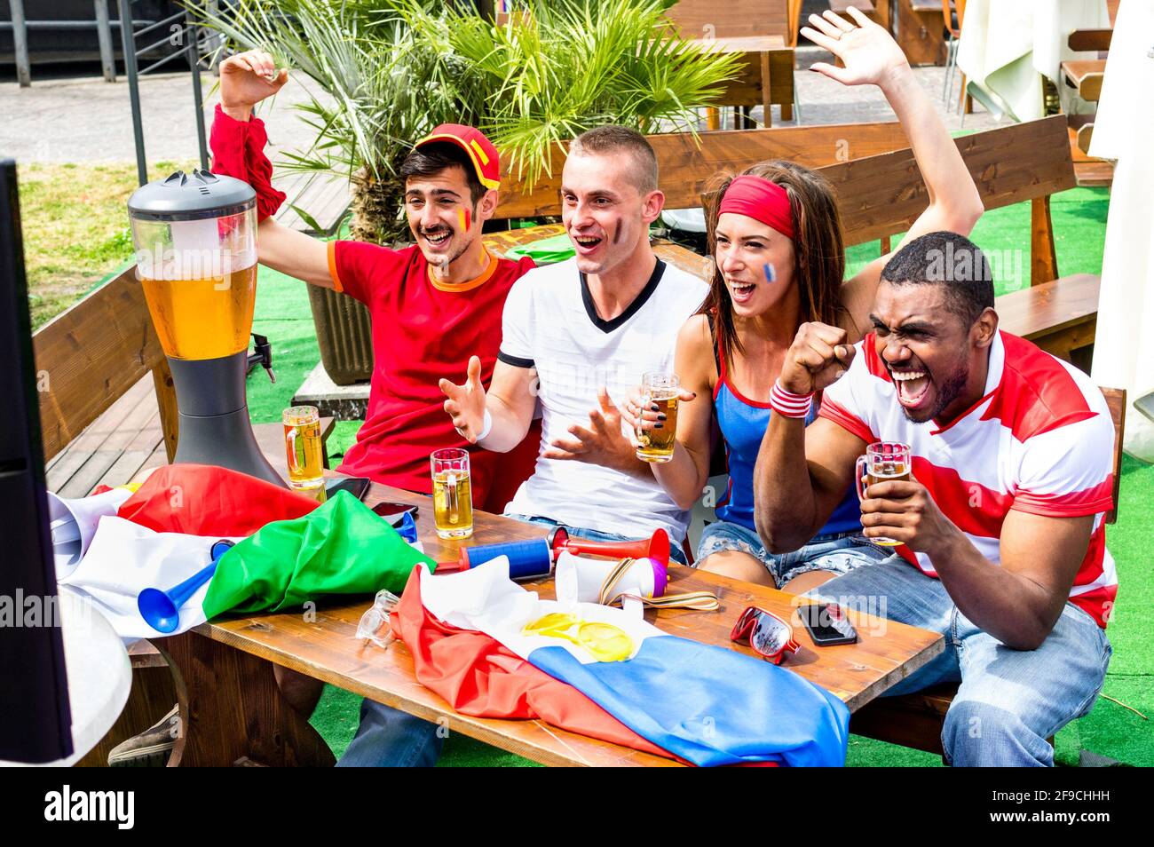 Young football supporter fans cheering with beer watching soccer match - Friends people with multicolored soccer tshirts and flags having fun Stock Photo