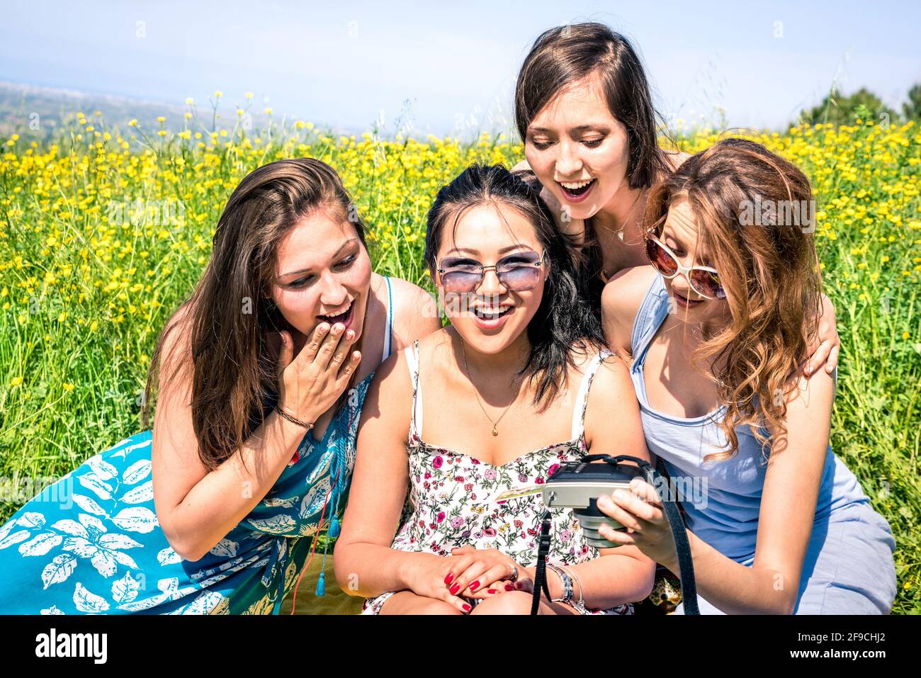 Multiracial girlfriends at countryside picnic watching photos in snapshot instant digital camera - Happy friendship fun concept with young people Stock Photo