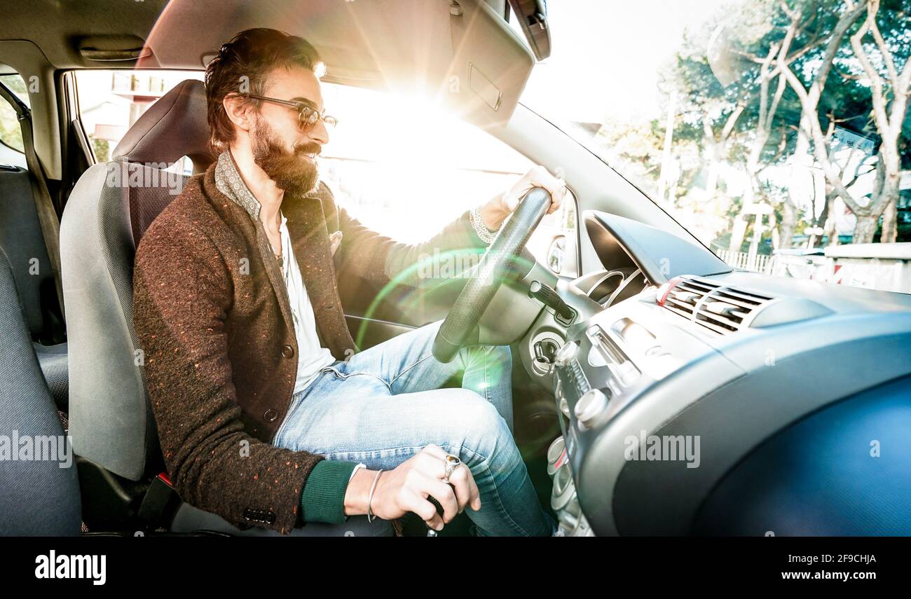 Young hipster fashion model driving car - Happy confident man with beard and alternative mustache smiling at business roadtrip - Lens flare halo Stock Photo