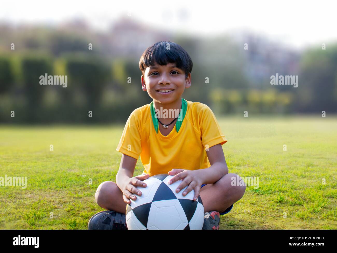 Young boy sitting in the ground holding soccer ball Stock Photo