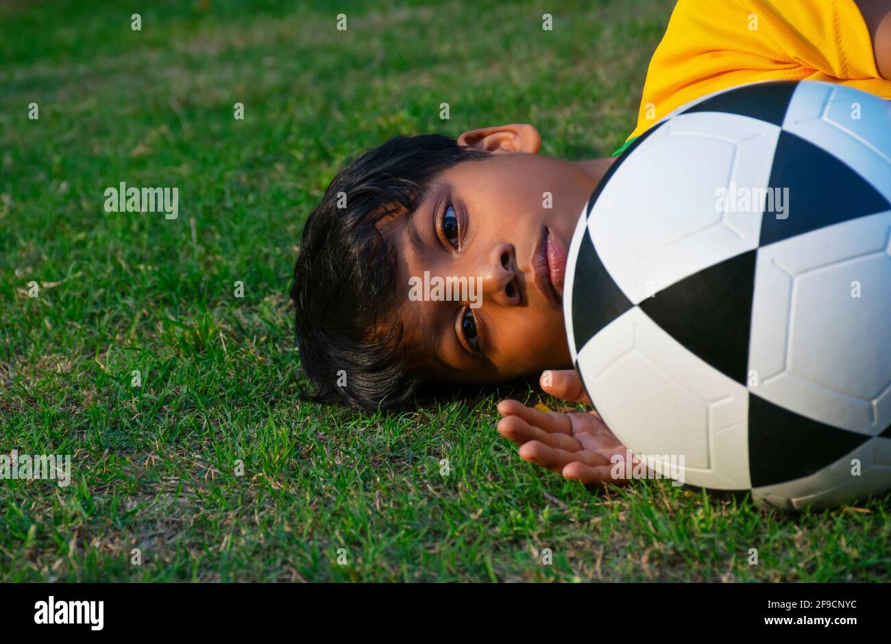 Young boy laying in the ground with football Stock Photo