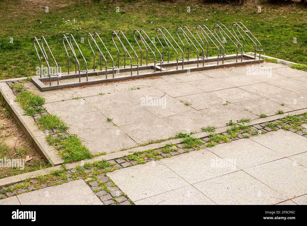 Empty bicycle park with steel slots on pavement next to green grass. Stock Photo