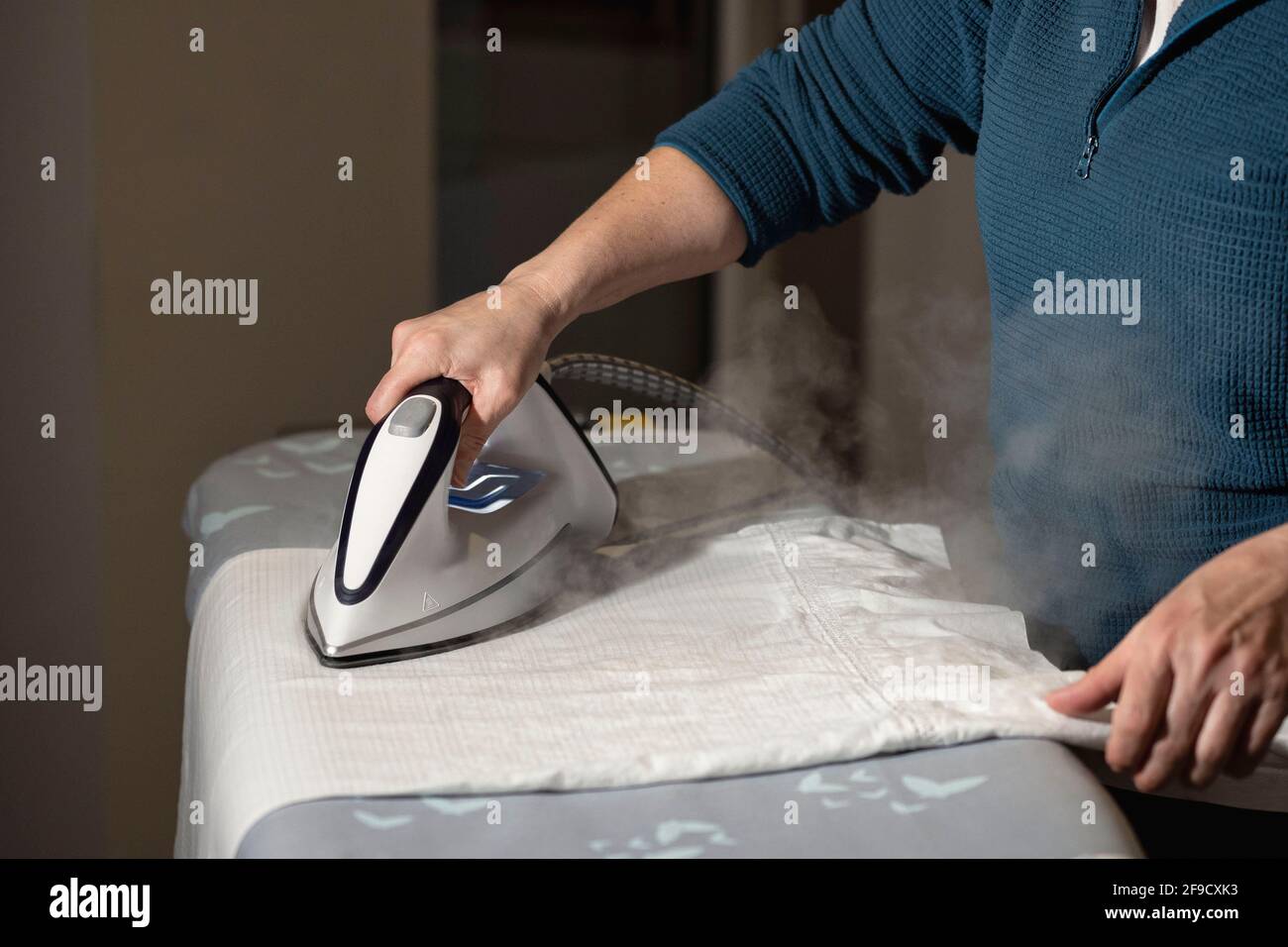 girl's hands holding steam iron and ironing linen garment Stock Photo
