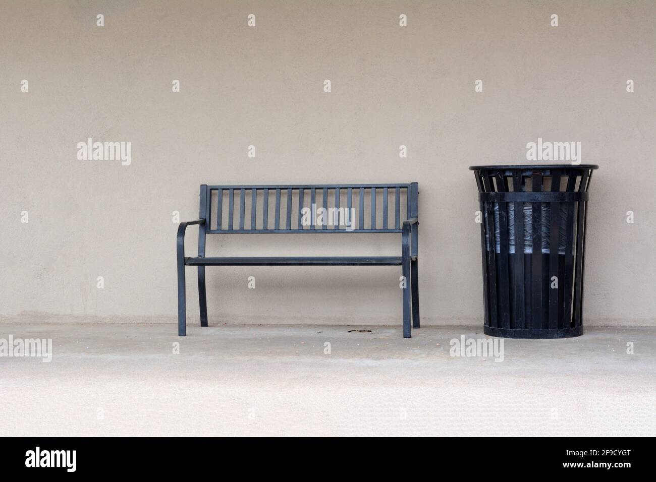 Urban bench and trash can in sidewalk against light brown office wall Stock Photo