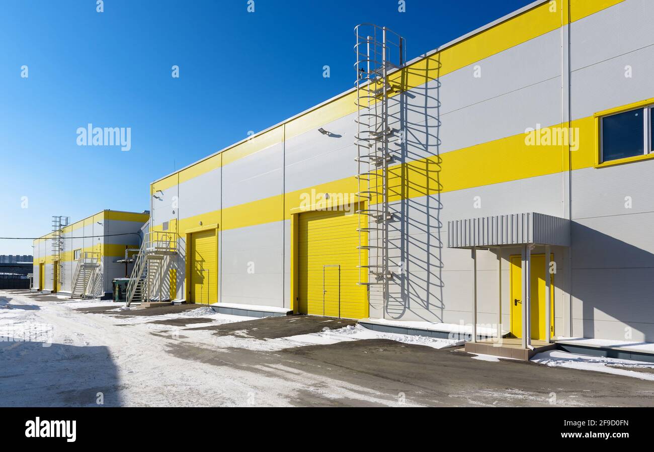 Modern warehouse exterior in winter, panorama of large yellow storehouse or mechanic shop. Big new commercial industrial buildings. Concept of contemp Stock Photo