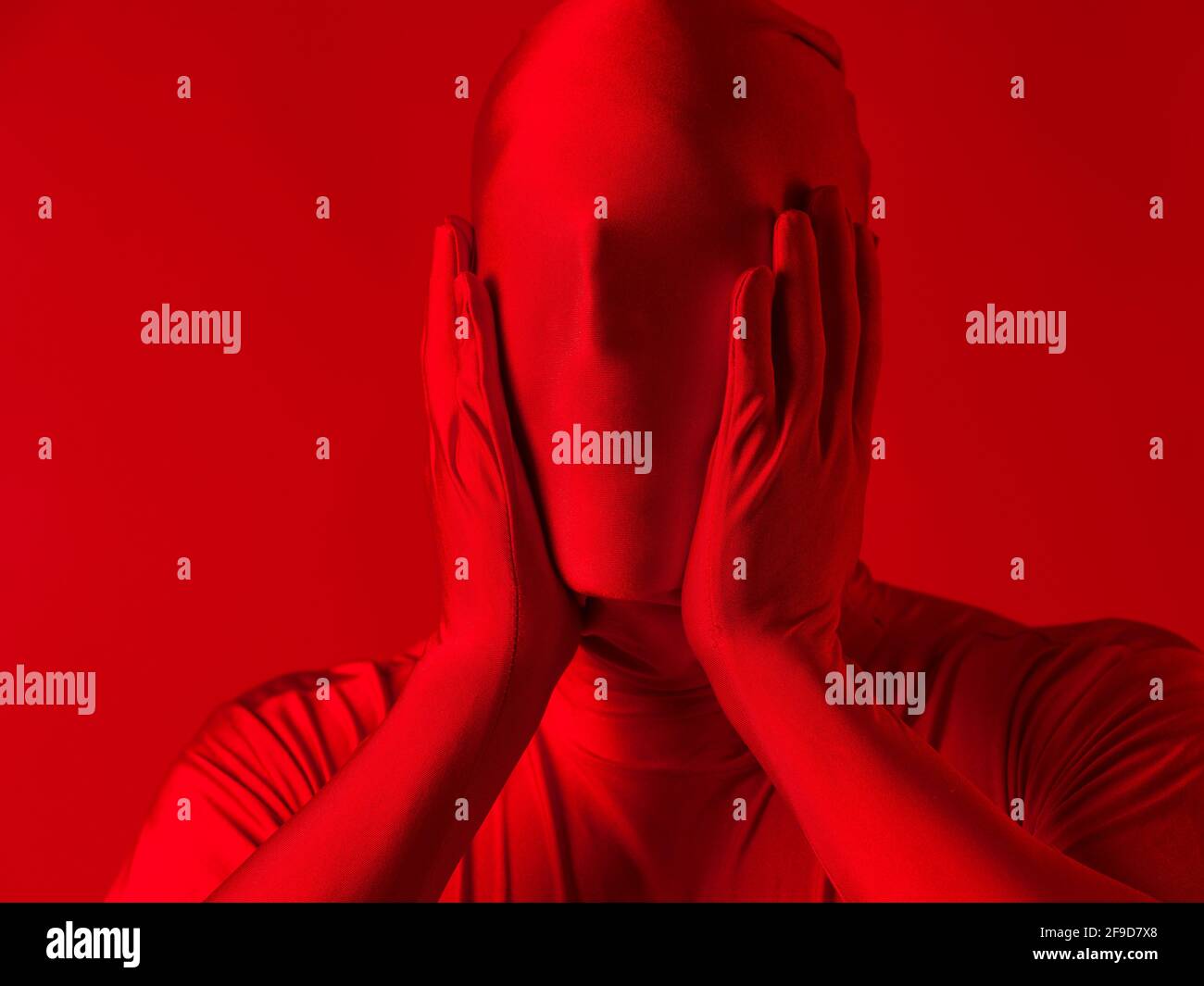 A screaming man in a red full suit, on a red background. The concept of pain and sadness and irritation. Stock Photo