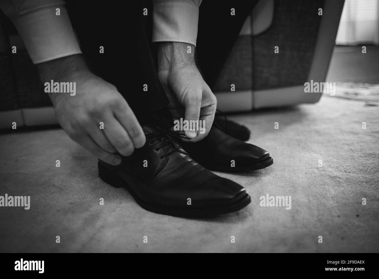 Grayscale shot of a man tying his leather shoes Stock Photo