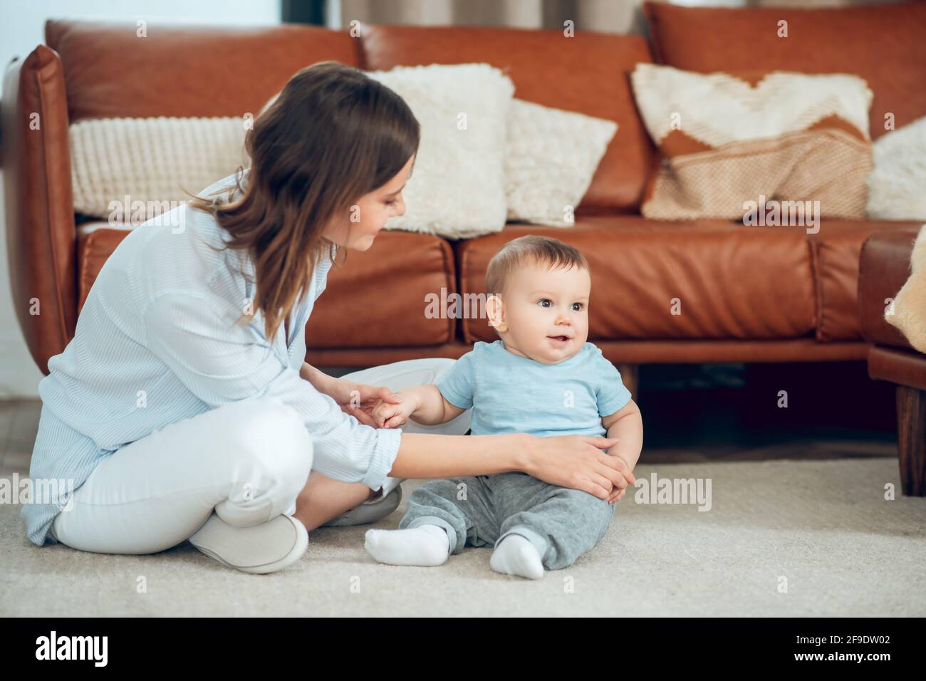 Attentive mother supporting child sitting on floor Stock Photo