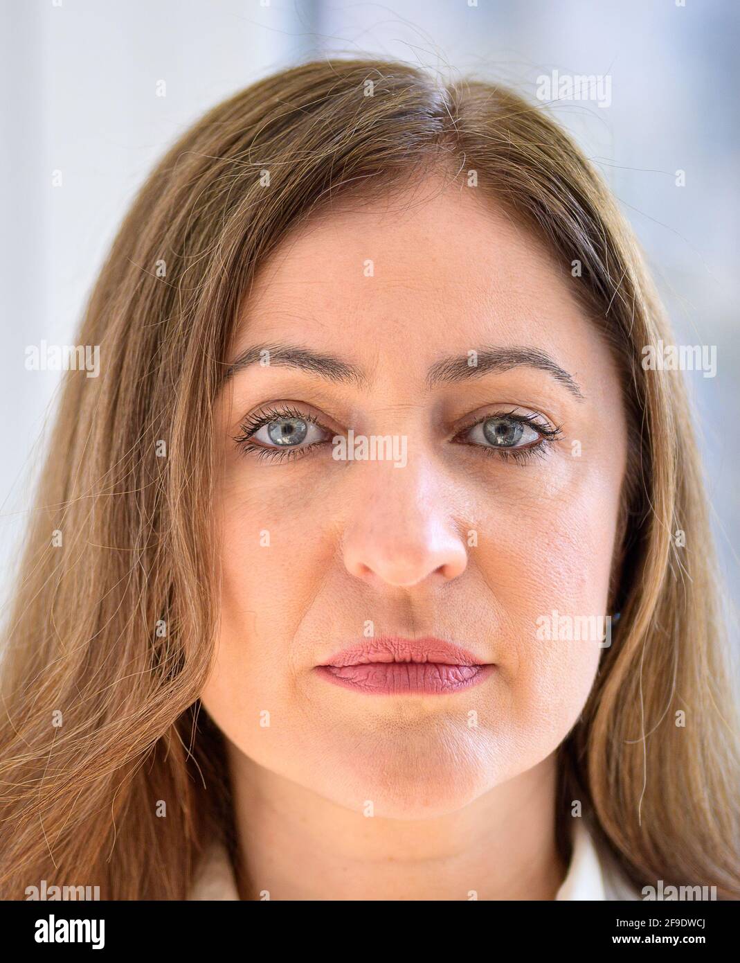 Head portrait of an attractive seriou middle-aged woman looking to the camera  with a contemplative expression in front of a window Stock Photo
