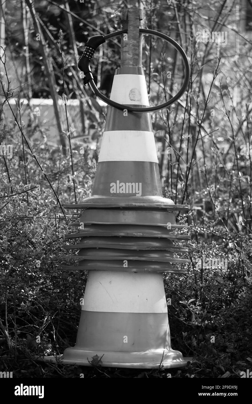 stacked and connected barrier pylons on a metal rod secured with a combination lock in black an white monochrome streetart Stock Photo