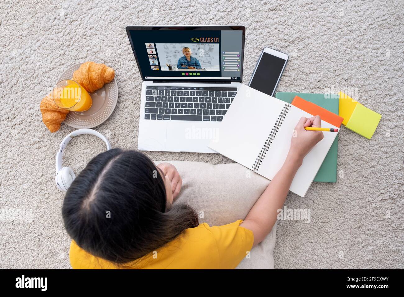 Asian female student video conference with teacher and friends using e-learing app on laptop computer at home.woman lying down on carpet.new normal le Stock Photo