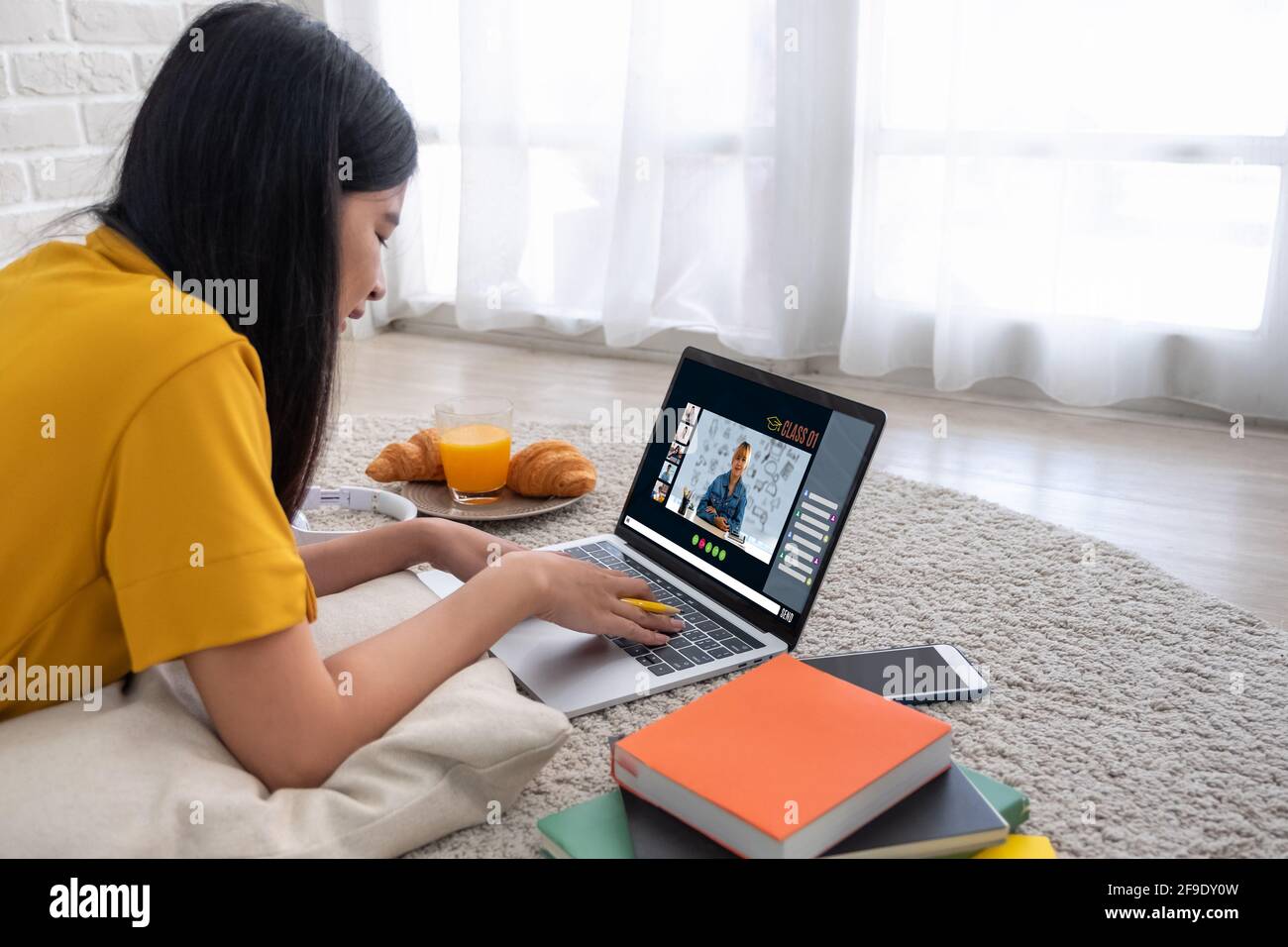 Asian female student video conference with teacher and friends using e-learing app on laptop computer at home.woman lying down on carpet.new normal le Stock Photo
