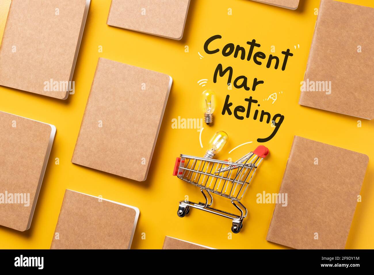 creativity content marketing concept,top view shopping cart with full of lightbulbs with Kraft paper book alignment in pattern on yellow desk surface. Stock Photo