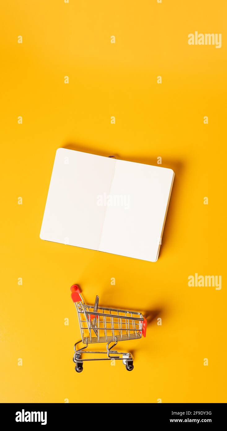 content marketing concept,top view oepn book with shopping cart on yellow desk surface.leave space for display your content.vertical background 9-16 r Stock Photo