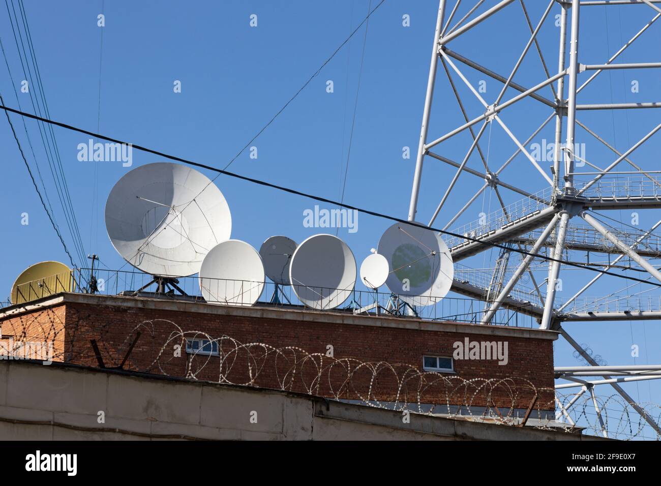 TV satellite dishes behind a fence with barbed wire Stock Photo