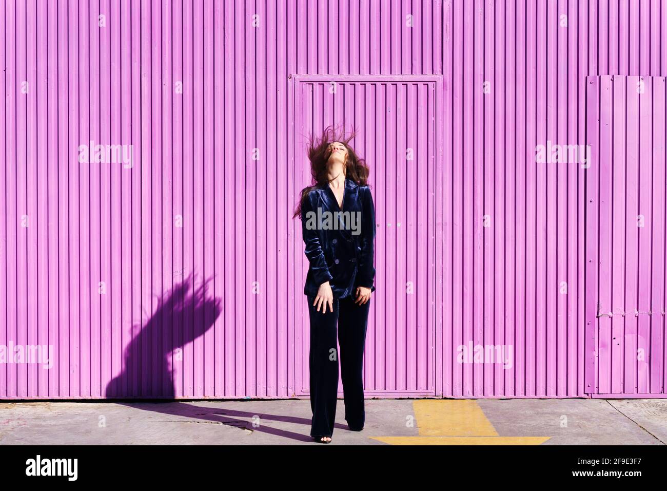 Woman wearing blue suit posing near pink shutter, moving her hair. Stock Photo