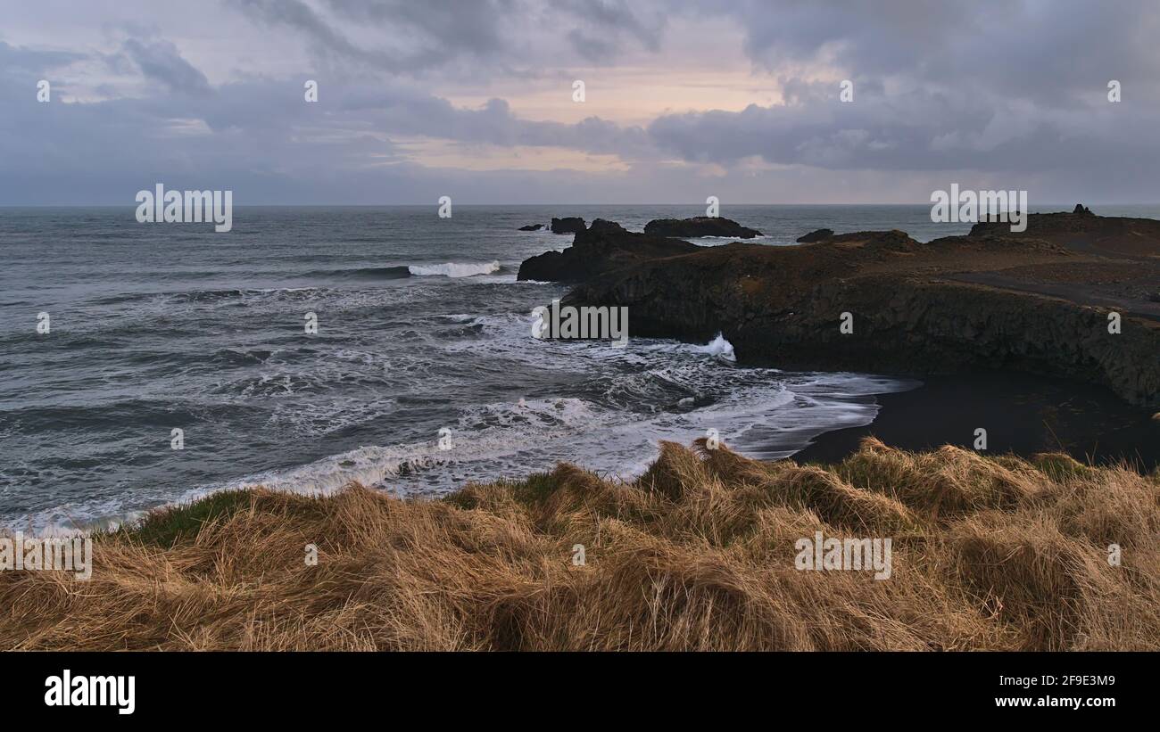 Beautiful view of the rough Atlantic coast of Dyrhólaey peninsula, southern Iceland with volcanic rocks, cliffs and a black sand beach in the evening. Stock Photo