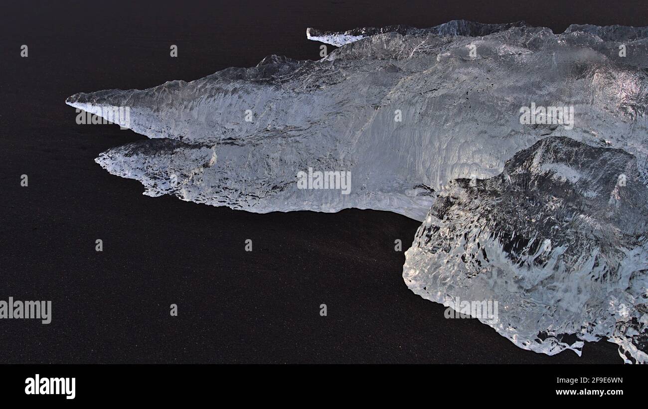 Closeup view of strange looking iceberg with beautiful ice surface shimmering in the evening sun in black sand of diamond beach in southern Iceland. Stock Photo