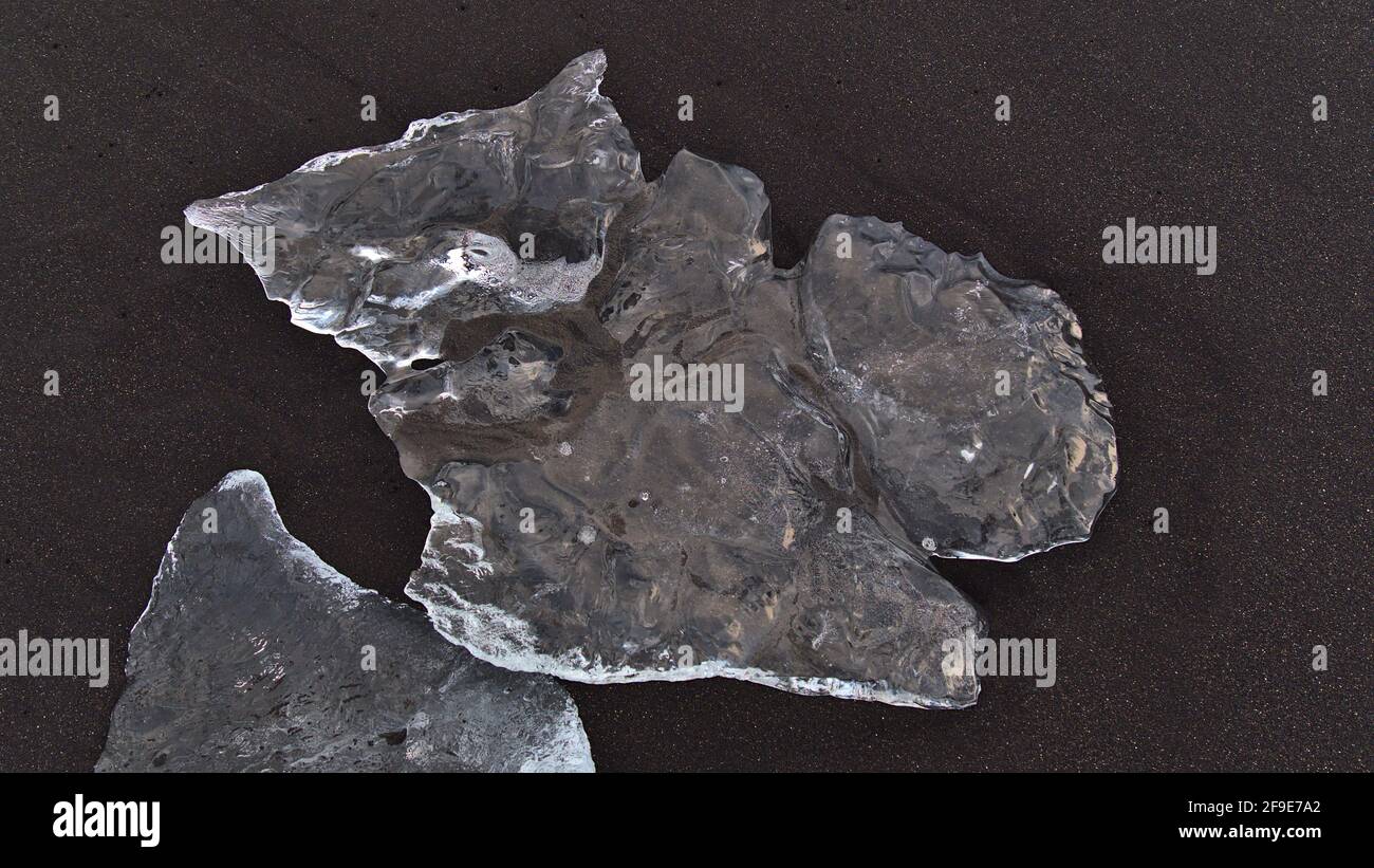 Close-up high angle view of small shimmering iceberg with beautiful clear ice surface in the black sand of diamond beach in southern Iceland. Stock Photo