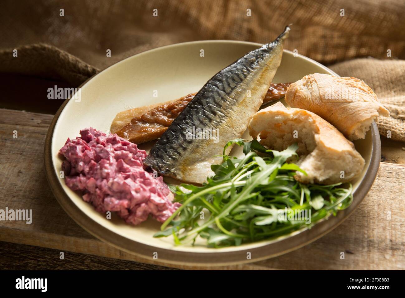 Two fillets of kiln roasted mackerel, Scomber scombrus, that have been served with a horseradish and pickled beetroot dressing, rocket salad and bread Stock Photo