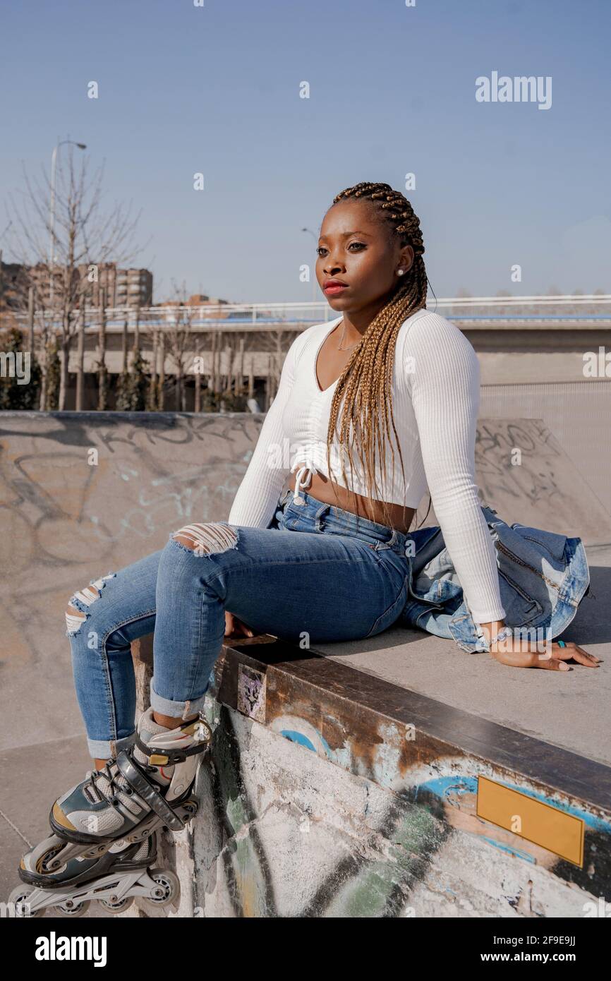 Cool black female with braided hairstyle and in rollerblades sitting on ...