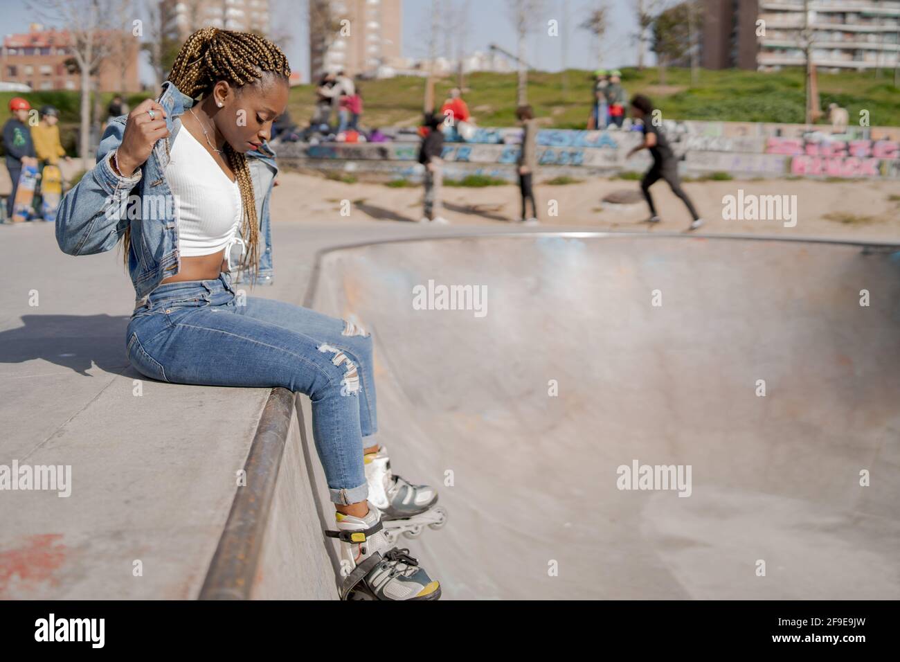 Cool black female with braided hairstyle and in rollerblades sitting on ...