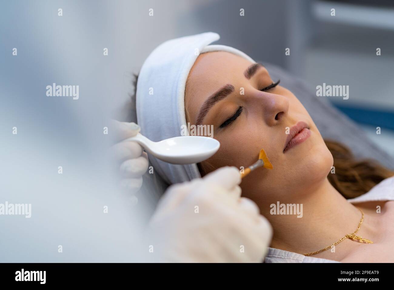 Anonymous crop cosmetologist applying acid peeling on face of female client during visit in beauty clinic Stock Photo