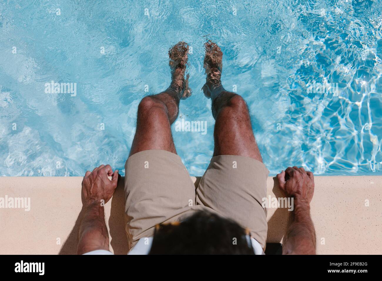 Top view of unrecognizable male freelancer sitting at poolside with legs in water during telework in summer Stock Photo