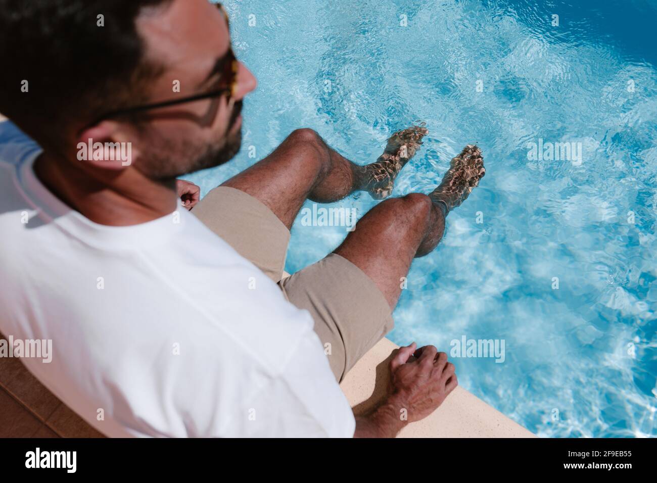 Top view of male freelancer sitting at poolside with legs in water during telework in summer Stock Photo
