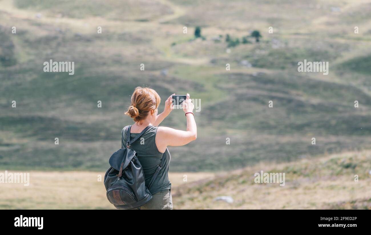 Back view of anonymous female backpacker taking photo of hills on ...