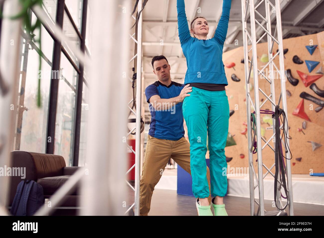 From below of female doing pull ups on horizontal bar with help of instructor while training in