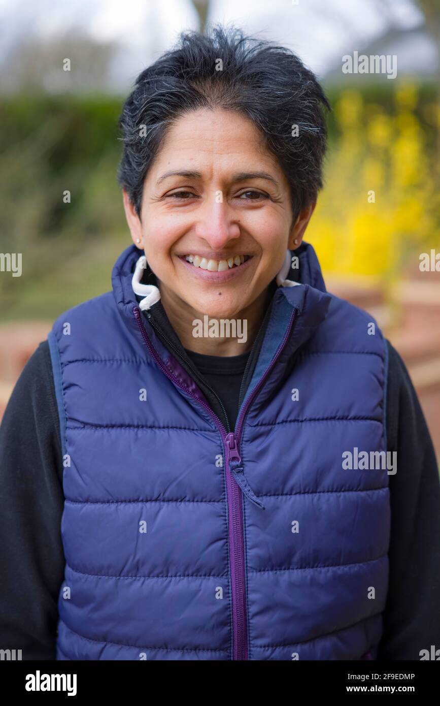 Asian Indian middle aged menopausal woman outdoors looking happy in England, UK Stock Photo