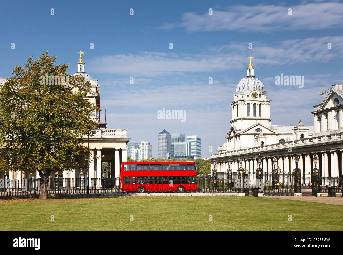 Red double decker bus in a central London scene. The Old Royal Naval College and National Maritime Museum in Greenwich Park. Canary Wharf skyline Stock Photo