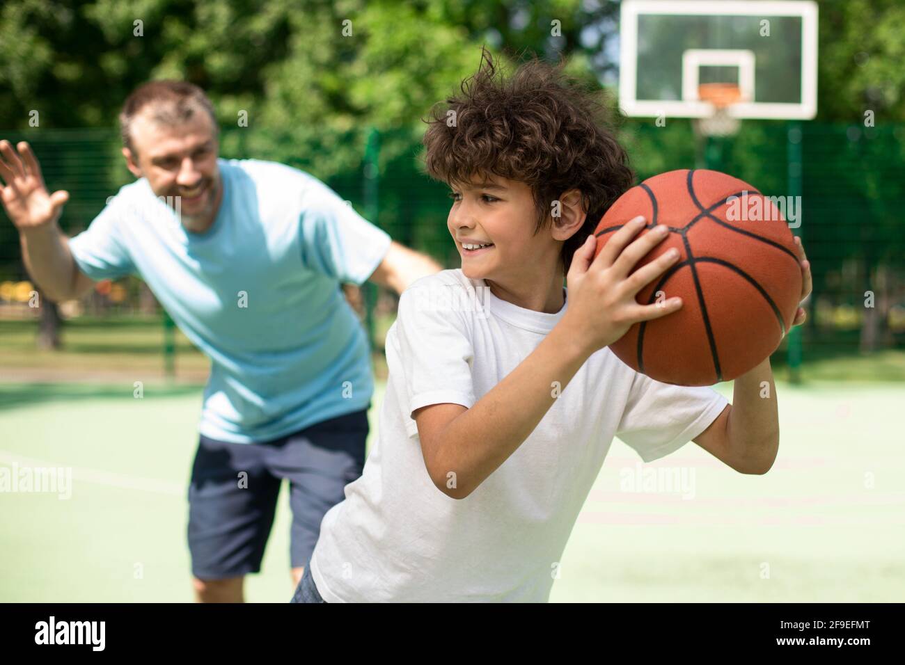Sportive dad teaching his son how to play basketball outside Stock