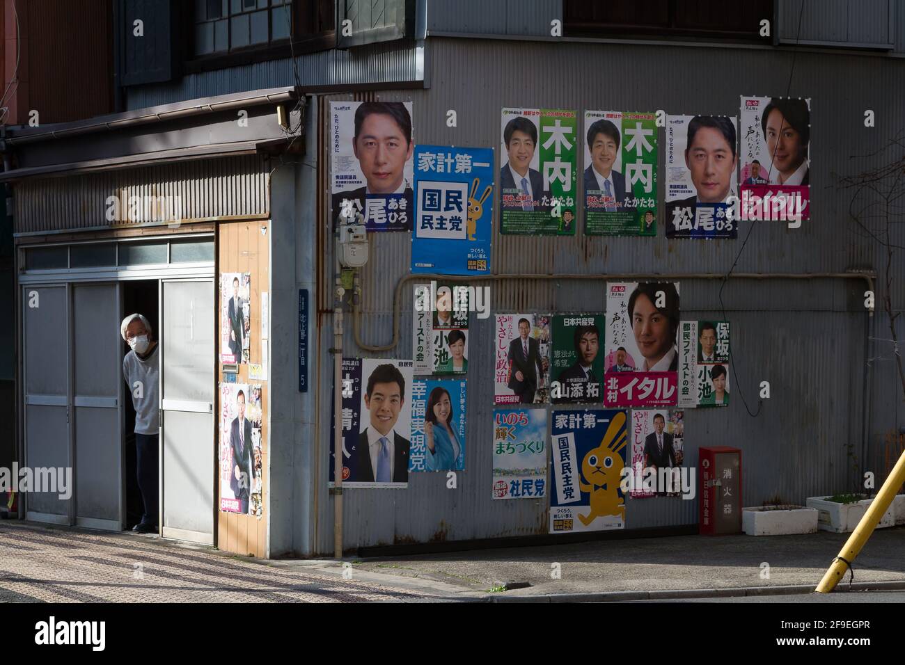 An older Japanese man looks out of a building with many political posters on its side. Ueno, Tokyo, Japan. Stock Photo