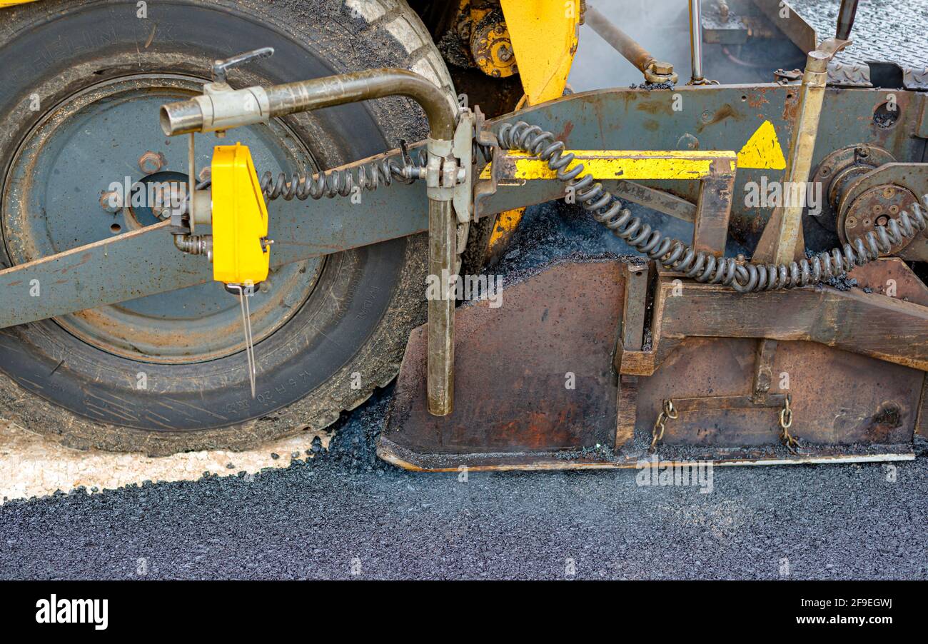 Worker regulate tracked paver laying asphalt heated to temperatures above 160 ° pavement on a runway Stock Photo