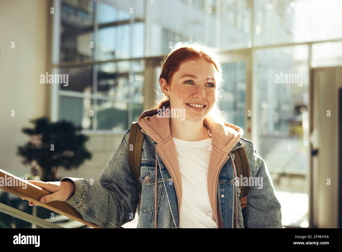 Female student standing in college and looking away. Happy young woman standing in college. Stock Photo