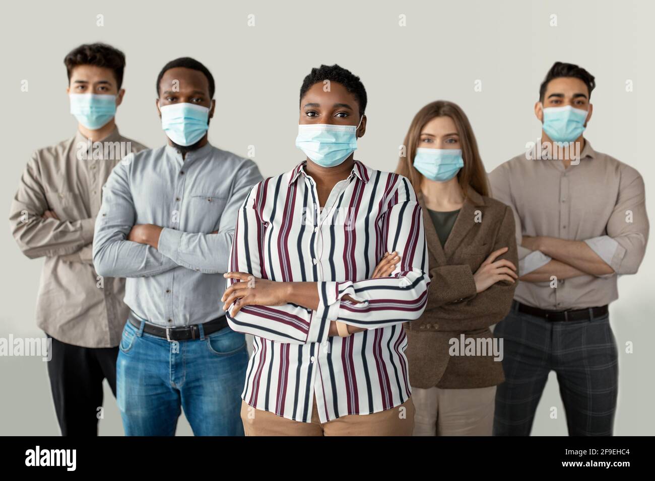 Multicultural businesspeople in masks standing in office with folded arms Stock Photo