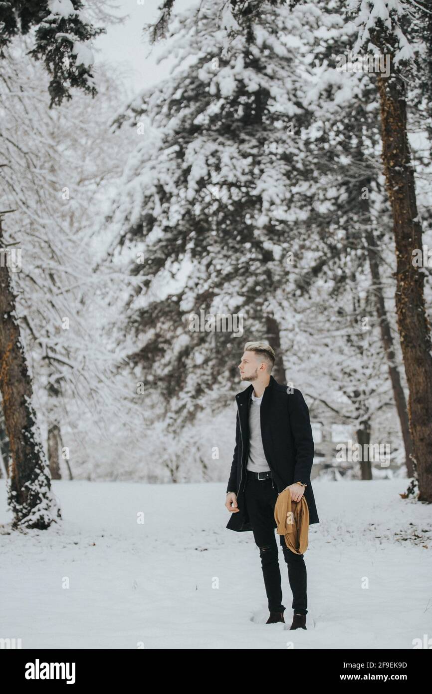 A handsome young man in a black winter outfit walking in a snowy forest ...