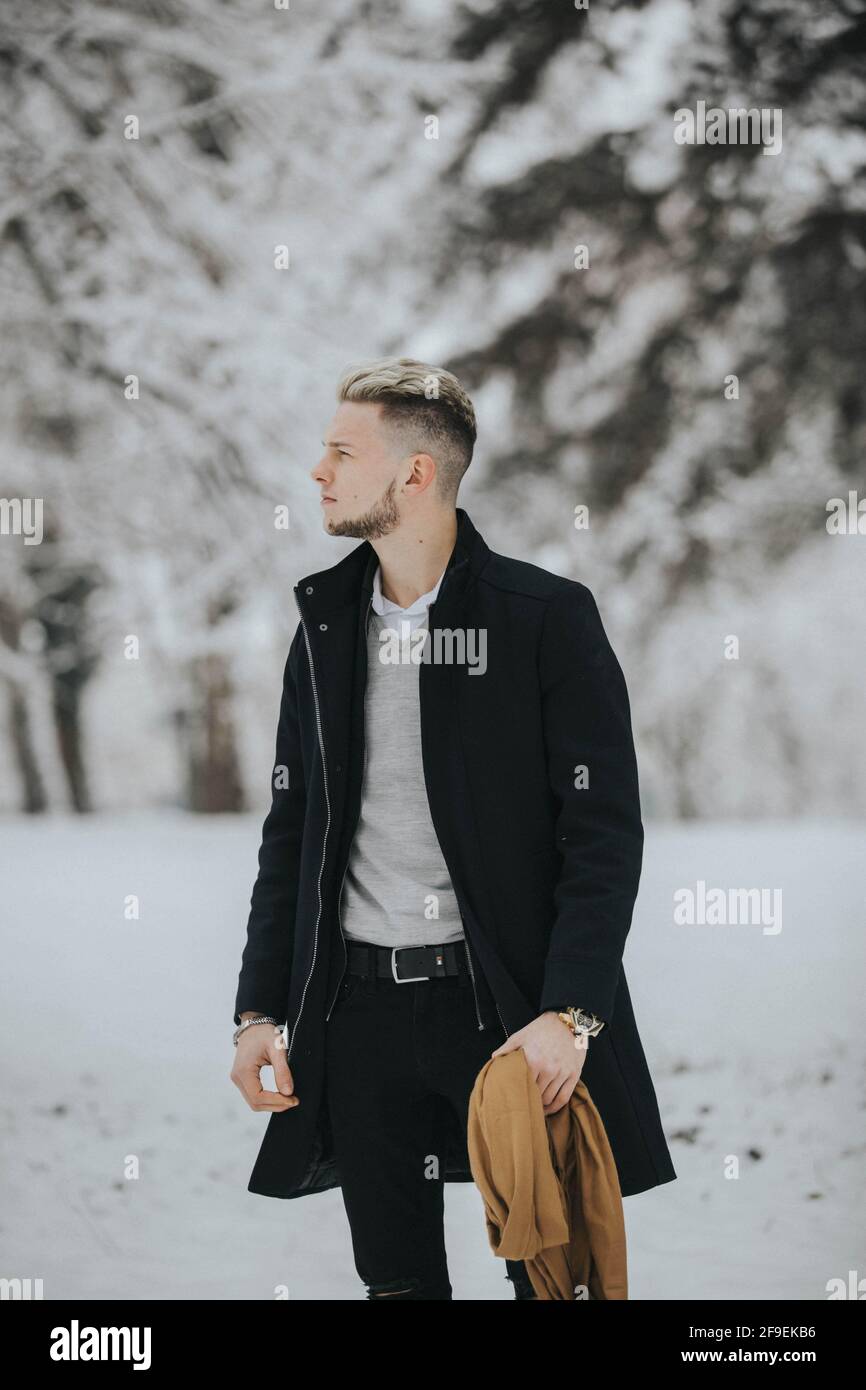 A handsome young man in a black winter outfit walking in a snowy forest ...