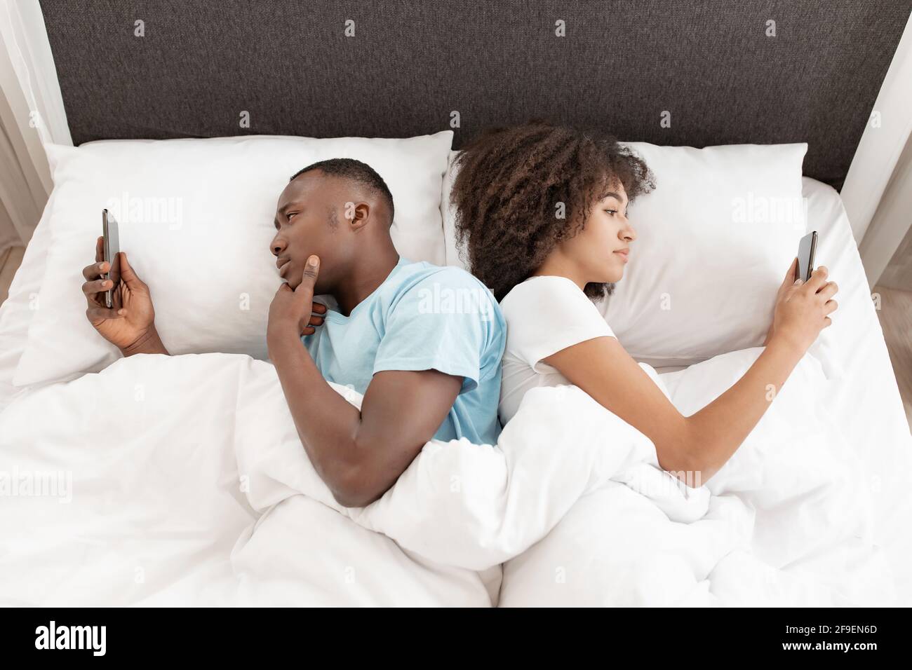 Awake using phone for chat, couple in quarrel, lying on bed back to back, using smartphones Stock Photo