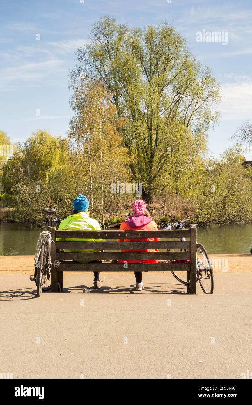Middle-aged cyclists sitting on a park bench enjoying the scenery, Barnes Pond, London, U.K. Stock Photo