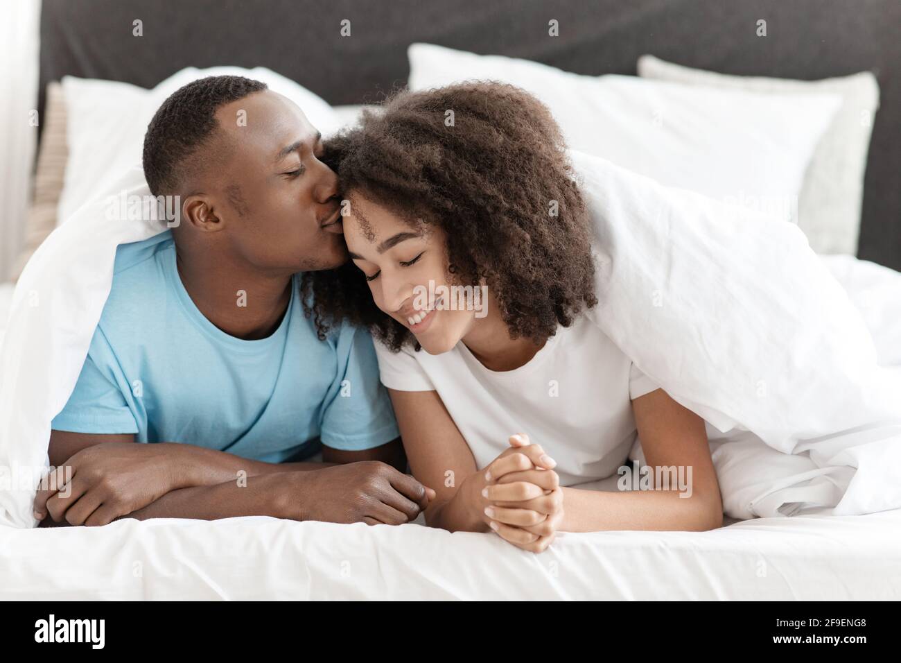 Lovely gentle cute smiling beautiful couple, under blanket in bed enjoying spare time at weekend