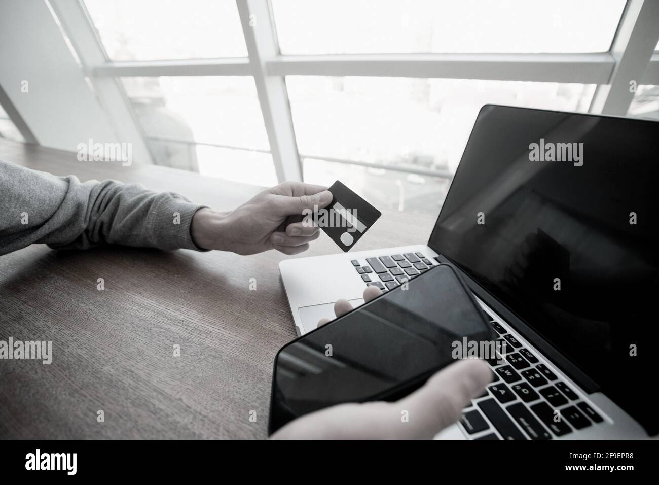 Male hands hold smartphone and credit card with laptop on background. Don't enter your credit card details on suspicious sites. Man using card to make Stock Photo