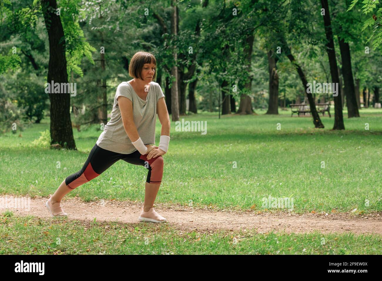 Female jogger stretching muscles and warming up for running exercise in park, selective focus Stock Photo