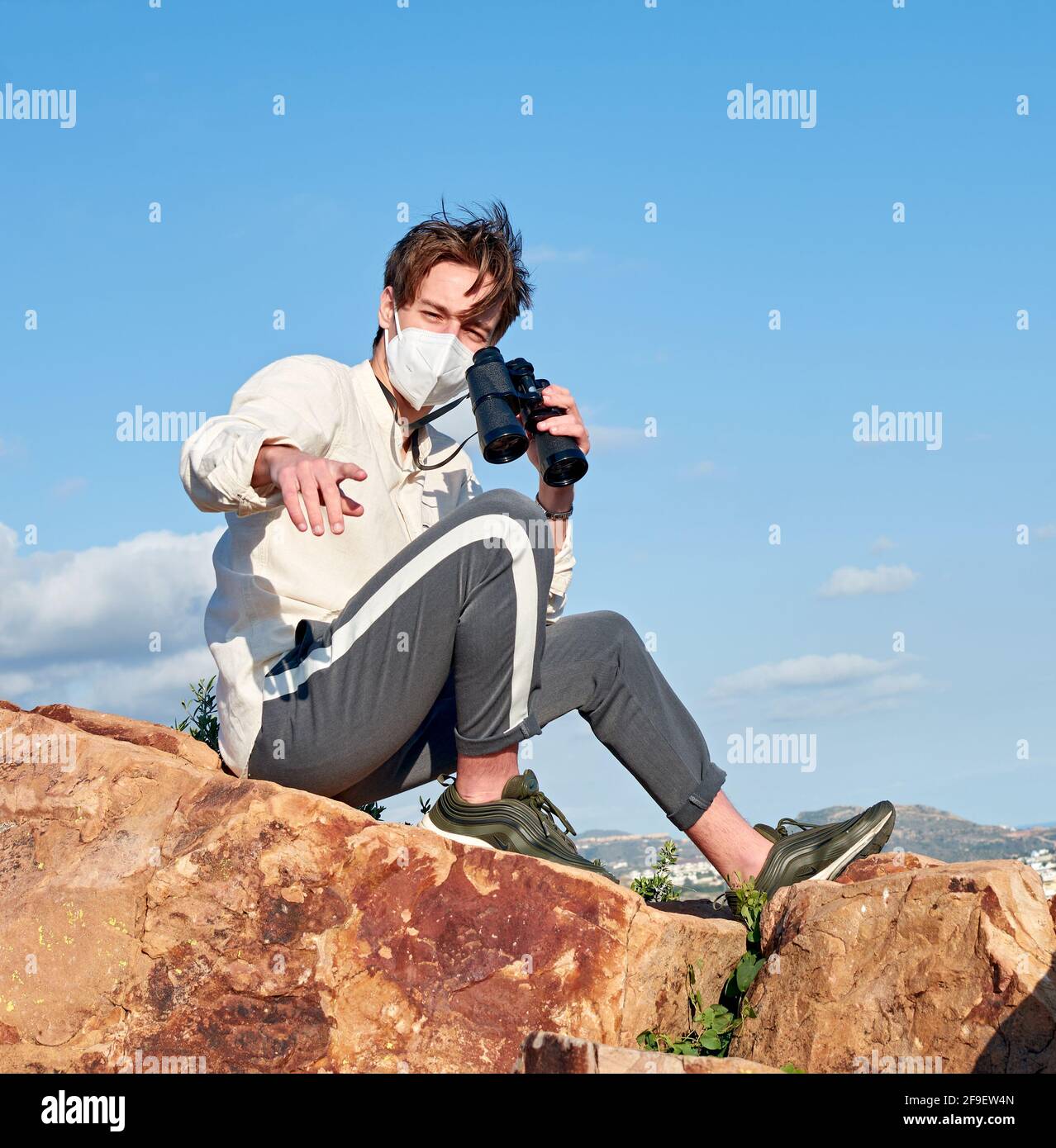 A Spanish adventurous male traveler wearing a mask sitting on a rock