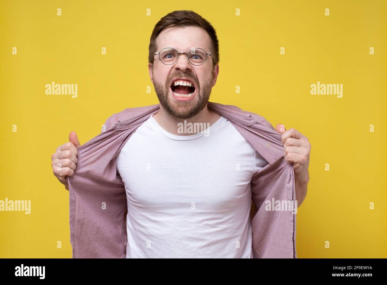 Angry, annoyed man looks furiously and bares teeth, grabbing his shirt with hands. Stress. Psychological concept.  Stock Photo