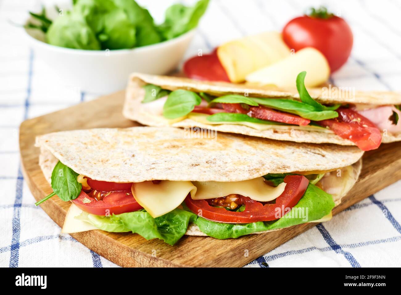 Piadina Romagnola with mozzarella cheese, tomatoes, ham and rocket salad on a cutting board. Italian flatbread or open sandwich. Selective focus. Stock Photo